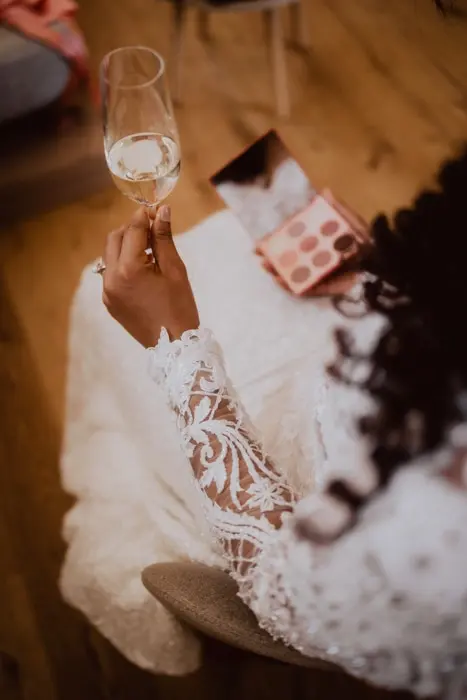 Hochzeitsfotograf Bayern Braut in Spitzenkleid mit Champagnerglas Dokumentarische Editorial Hochzeitsfotografie