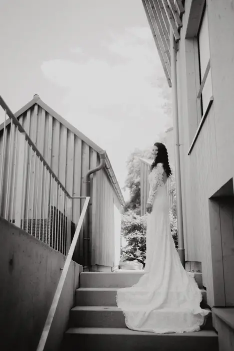 Hochzeitsfotograf Bayern Braut in einem langen weißen Kleid auf einer Treppe im Freien Dokumentarische Editorial Hochzeitsfotografie