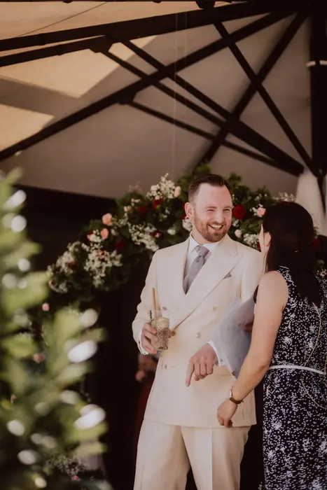 Hochzeitsfotograf Bayern Mann im cremefarbenen Anzug bei einer Feier unterhält sich mit einer Frau Dokumentarische Editorial Hochzeitsfotografie