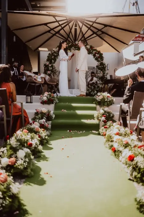 Hochzeitsfotograf Bayern Hochzeitspaar auf grünem Gang mit Blumen und Publikum Dokumentarische Editorial Hochzeitsfotografie