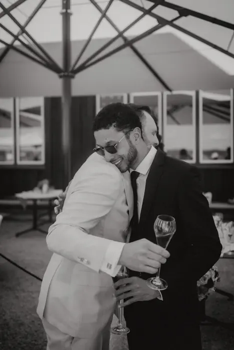 Hochzeitsfotograf Bayern Zwei Männer in Anzügen umarmen sich bei einer Feier Dokumentarische Editorial Hochzeitsfotografie