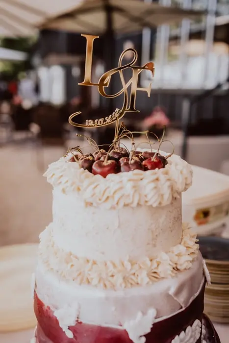 Hochzeitsfotograf Bayern Hochzeitstorte mit Initialen-Topper und Kirschen Dokumentarische Editorial Hochzeitsfotografie