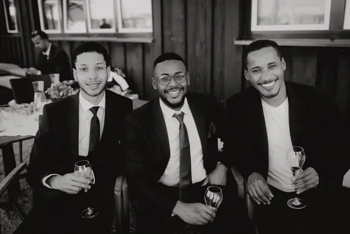Hochzeitsfotograf Bayern Drei Männer in Anzügen lachen und halten Sektgläser Dokumentarische Editorial Hochzeitsfotografie