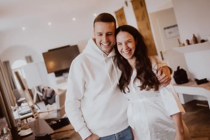 Hochzeitsfotograf Bayern Lächelndes Paar umarmt sich in modernem Wohnzimmer Dokumentarische Editorial Hochzeitsfotografie