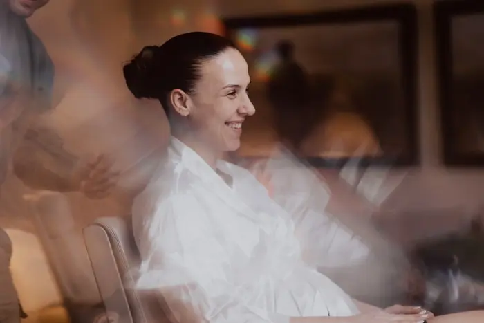 Hochzeitsfotograf Bayern Frau lächelt entspannt in einem Friseursalon Dokumentarische Editorial Hochzeitsfotografie