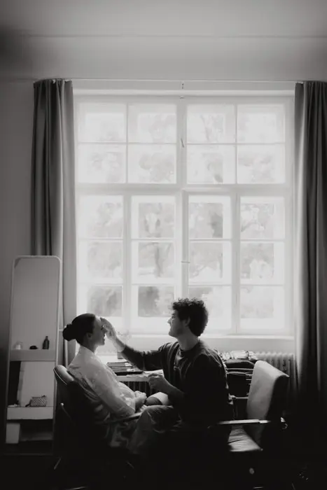 Hochzeitsfotograf Bayern Zwei Personen im Wohnzimmer bei natürlichem Licht, eine schminkt die andere Dokumentarische Editorial Hochzeitsfotografie
