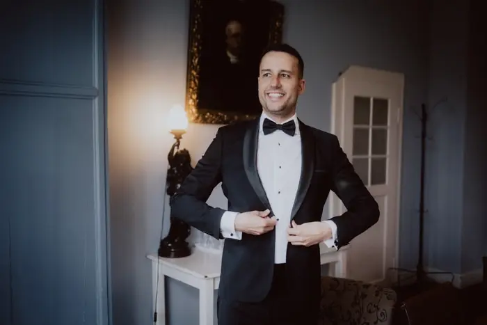 Hochzeitsfotograf Bayern Eleganter Mann im Smoking lächelt in stilvollem Raum Dokumentarische Editorial Hochzeitsfotografie