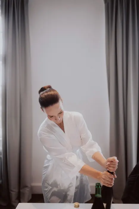 Hochzeitsfotograf Bayern Frau in Bademantel öffnet Sektflasche Dokumentarische Editorial Hochzeitsfotografie