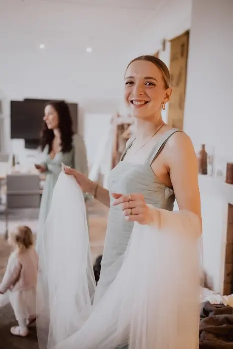 Hochzeitsfotograf Bayern Lächelnde Brautjungfer im grünen Kleid mit Schleier im Wohnraum Dokumentarische Editorial Hochzeitsfotografie