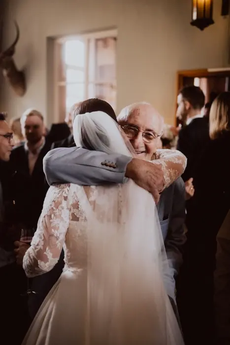 Hochzeitsfotograf Bayern Braut umarmt älteren Mann bei Hochzeitsempfang Dokumentarische Editorial Hochzeitsfotografie