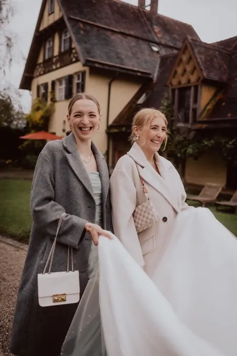 Hochzeitsfotograf Bayern Zwei elegant gekleidete Frauen vor einem alten Landhaus Dokumentarische Editorial Hochzeitsfotografie