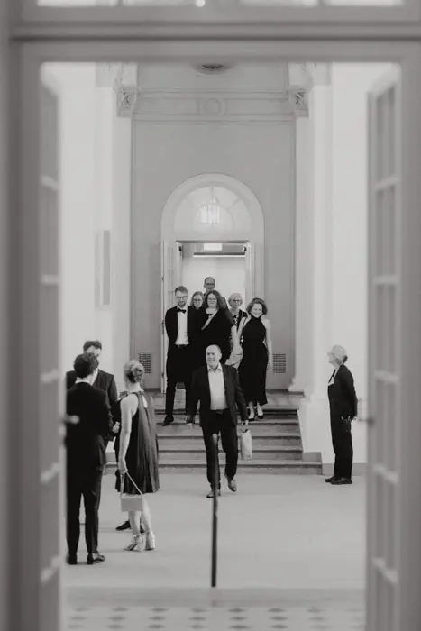 Hochzeitsfotograf Bayern Schwarz-Weiß-Foto von elegant gekleideten Menschen in einem stilvollen Gebäude Dokumentarische Editorial Hochzeitsfotografie