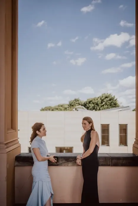 Hochzeitsfotograf Bayern Zwei Frauen in eleganter Kleidung auf einer Terrasse mit blauem Himmel Dokumentarische Editorial Hochzeitsfotografie