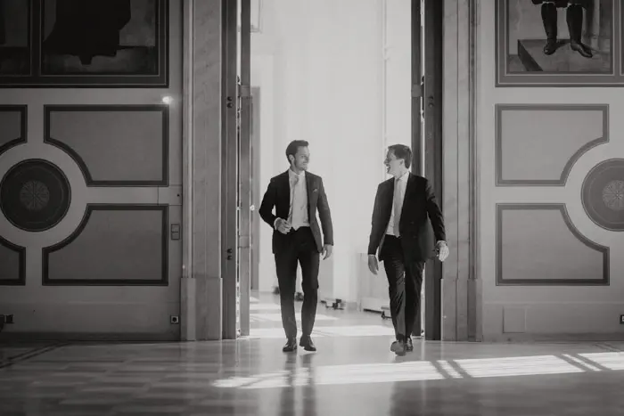 Hochzeitsfotograf Bayern Männer in Anzügen spazieren in elegantem Gebäude mit offenen Türen Dokumentarische Editorial Hochzeitsfotografie