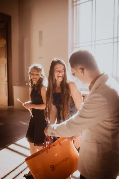 Hochzeitsfotograf Bayern Gruppe von Menschen bei einem sonnigen Event mit Einkaufstasche Dokumentarische Editorial Hochzeitsfotografie