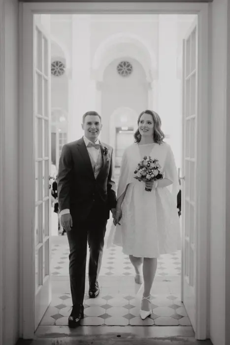 Hochzeitsfotograf Bayern Schwarzweißfoto von einem Hochzeitspaar, das durch geöffnete Türen schreitet Dokumentarische Editorial Hochzeitsfotografie