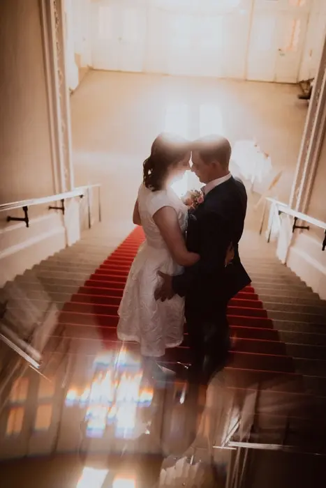 Hochzeitsfotograf Bayern Brautpaar umarmt sich auf einer Treppe mit rotem Teppich Dokumentarische Editorial Hochzeitsfotografie