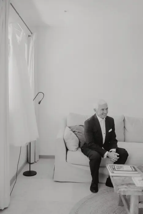 Hochzeitsfotograf Bayern Schwarzweißfoto eines Mannes im Anzug, der auf einem Sofa sitzt Dokumentarische Editorial Hochzeitsfotografie