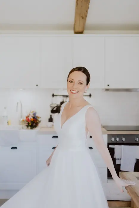 Hochzeitsfotograf Bayern Braut in elegantem weißen Kleid in moderner Küche Dokumentarische Editorial Hochzeitsfotografie