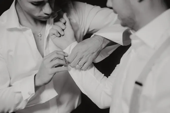 Hochzeitsfotograf Bayern Zwei Männer in weißen Hemden, einer hilft dem anderen beim Manschettenknöpfe anlegen Dokumentarische Editorial Hochzeitsfotografie