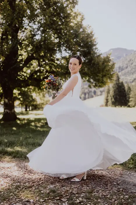 Hochzeitsfotograf Bayern Braut tanzt im weißen Kleid in malerischer Landschaft Dokumentarische Editorial Hochzeitsfotografie