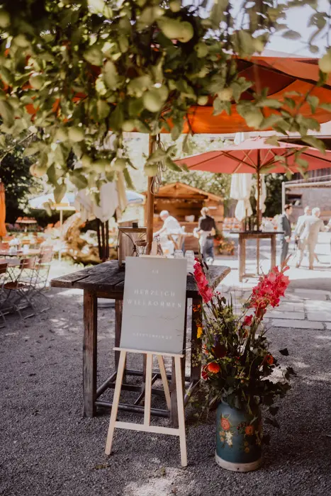 Hochzeitsfotograf Bayern Gemütlicher Außenbereich mit grüner Tafel und roten Sonnenschirmen Dokumentarische Editorial Hochzeitsfotografie