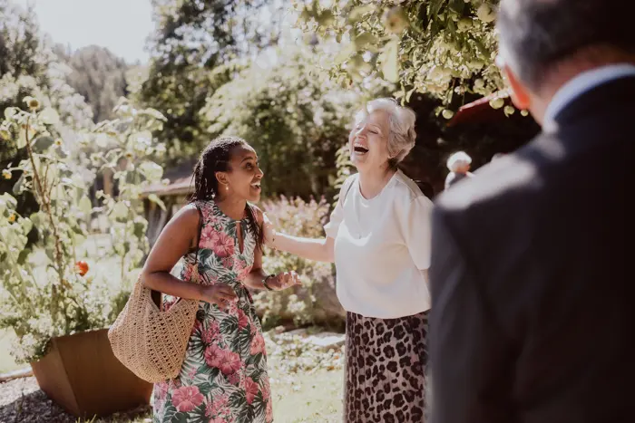 Hochzeitsfotograf Bayern Zwei lachende Frauen im Sommergarten bei einem Gespräch Dokumentarische Editorial Hochzeitsfotografie
