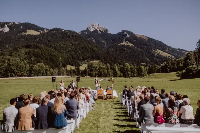 Hochzeitsfotograf Bayern Hochzeitszeremonie im Freien mit Bergblick und zahlreichen Gästen Dokumentarische Editorial Hochzeitsfotografie