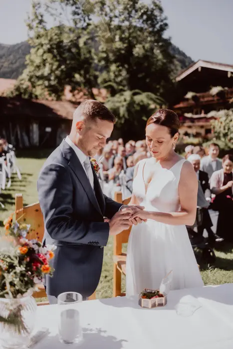 Hochzeitsfotograf Bayern Brautpaar tauscht Ringe bei Zeremonie im Freien vor Gästen Dokumentarische Editorial Hochzeitsfotografie