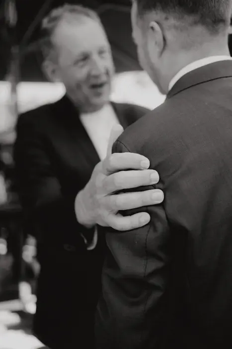 Hochzeitsfotograf Bayern Zwei Männer in Anzügen unterhalten sich herzlich Dokumentarische Editorial Hochzeitsfotografie