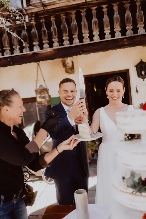 Hochzeitsfotograf Bayern Hochzeitspaar schneidet Torte bei rustikaler Feier an Dokumentarische Editorial Hochzeitsfotografie