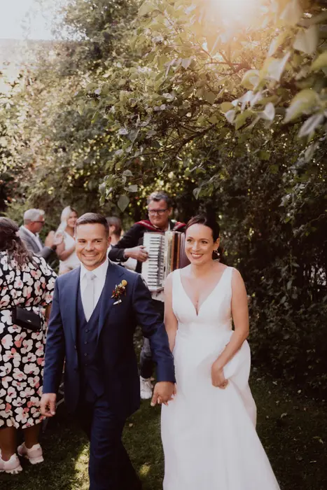 Hochzeitsfotograf Bayern Hochzeitspaar spaziert im Garten, von Akkordeonmusik begleitet Dokumentarische Editorial Hochzeitsfotografie