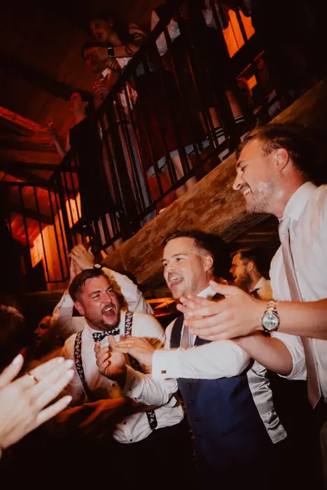 Hochzeitsfotograf Bayern Lachende Männer bei einer Hochzeitsfeier in einem festlichen Saal Dokumentarische Editorial Hochzeitsfotografie
