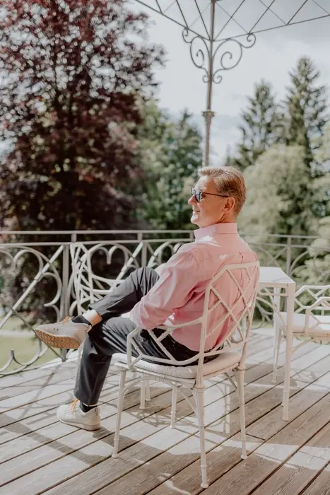 Hochzeitsfotograf Bayern Mann in rosa Hemd entspannt auf Balkon mit Naturkulisse Dokumentarische Editorial Hochzeitsfotografie