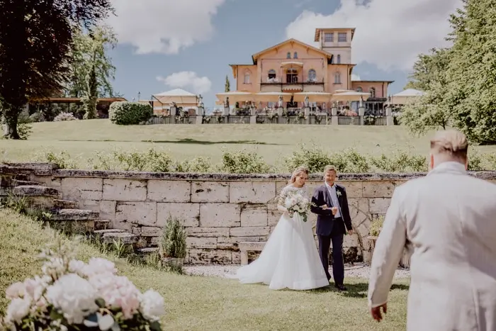 Hochzeitsfotograf Bayern Brautpaar bei Hochzeit im Freien vor Villa mit blauen Himmel Dokumentarische Editorial Hochzeitsfotografie