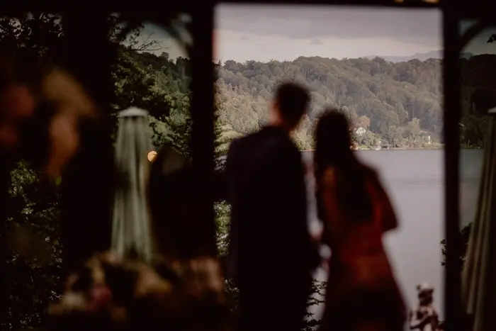 Hochzeitsfotograf Bayern Verschwommenes Paar blickt auf bewaldete Landschaft und See bei Sonnenuntergang Dokumentarische Editorial Hochzeitsfotografie