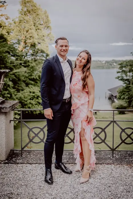 Hochzeitsfotograf Bayern Paar posiert auf Balkon mit Seeblick, lächelnd Dokumentarische Editorial Hochzeitsfotografie