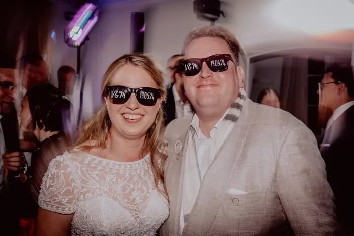 Hochzeitsfotograf Bayern Glückliches Paar auf einer Party mit Sonnenbrillen und lächelnd Dokumentarische Editorial Hochzeitsfotografie