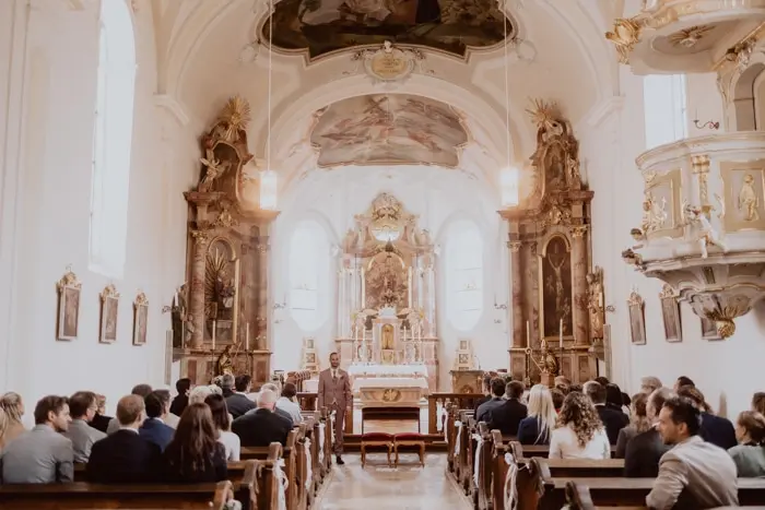 Hochzeitsfotograf Bayern Innenansicht einer schönen alten Kirche mit versammelter Gemeinde Dokumentarische Editorial Hochzeitsfotografie
