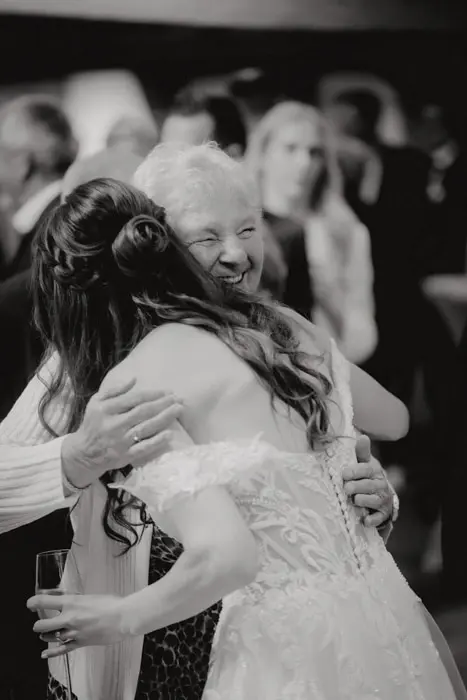 Hochzeitsfotograf Bayern Schwarzweißaufnahme von zwei Frauen, die sich auf einer Feier umarmen Dokumentarische Editorial Hochzeitsfotografie