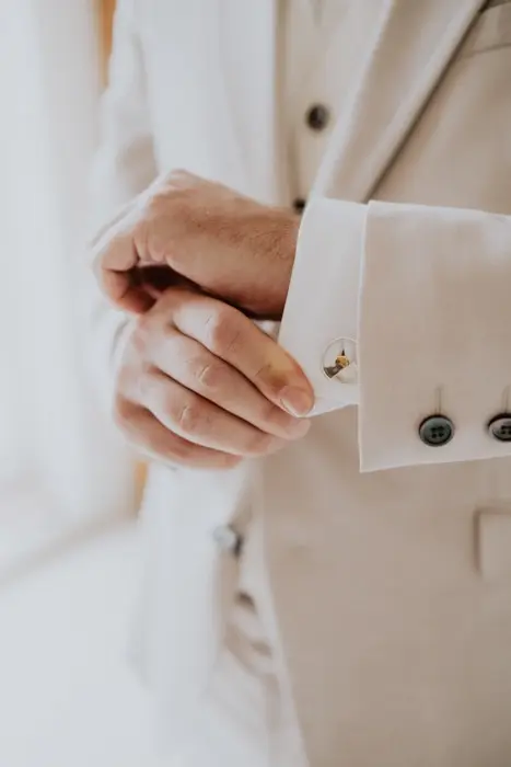 Hochzeitsfotograf Bayern Nahaufnahme eines Mannes im Anzug, der Manschettenknöpfe anlegt Dokumentarische Editorial Hochzeitsfotografie