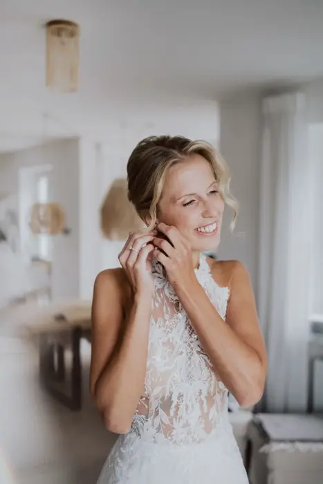 Hochzeitsfotograf Bayern Braut zieht Ohrringe vor Hochzeit im sonnendurchfluteten Raum an Dokumentarische Editorial Hochzeitsfotografie