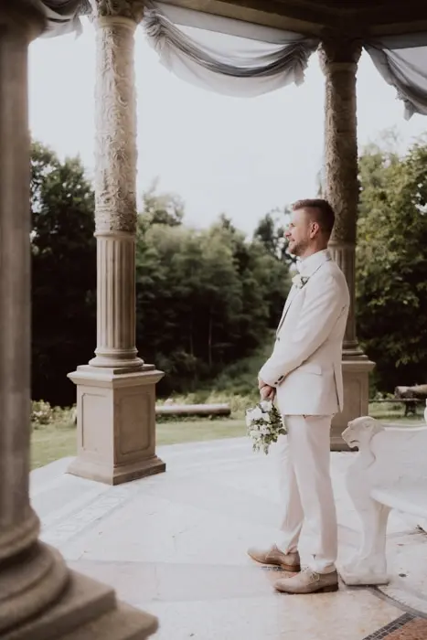 Hochzeitsfotograf Bayern Bräutigam in weißem Anzug bei Hochzeit in Pavillon stehend Dokumentarische Editorial Hochzeitsfotografie