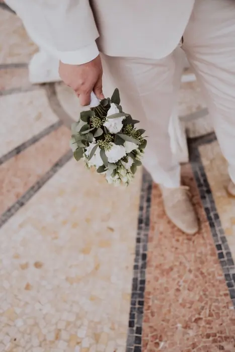 Hochzeitsfotograf Bayern Bräutigam in hellem Anzug mit Blumenstrauß auf Mosaikboden Dokumentarische Editorial Hochzeitsfotografie