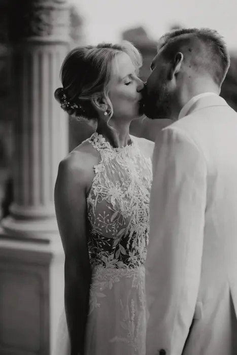 Hochzeitsfotograf Bayern Brautpaar im eleganten Hochzeitsgewand bei romantischem Kuss Dokumentarische Editorial Hochzeitsfotografie