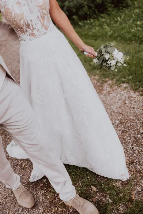 Hochzeitsfotograf Bayern Brautpaar in eleganter Hochzeitskleidung auf Schotterweg Dokumentarische Editorial Hochzeitsfotografie