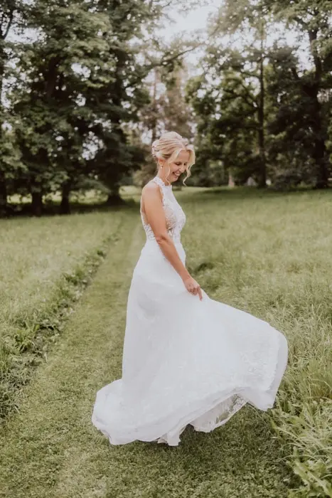 Hochzeitsfotograf Bayern Braut in weißem Kleid dreht sich auf einem grünen Weg im Park Dokumentarische Editorial Hochzeitsfotografie