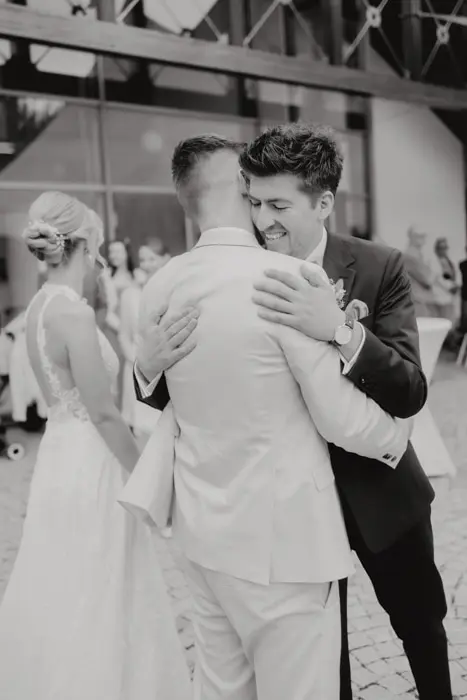 Hochzeitsfotograf Bayern Schwarzweißfoto von Gästen, die sich auf einer Hochzeit umarmen Dokumentarische Editorial Hochzeitsfotografie