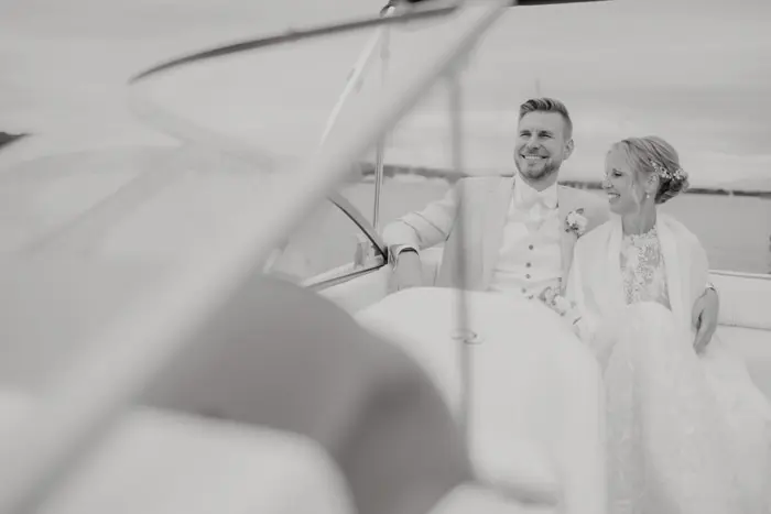 Hochzeitsfotograf Bayern Brautpaar in einem Boot, lächelnd nebeneinander sitzend Dokumentarische Editorial Hochzeitsfotografie