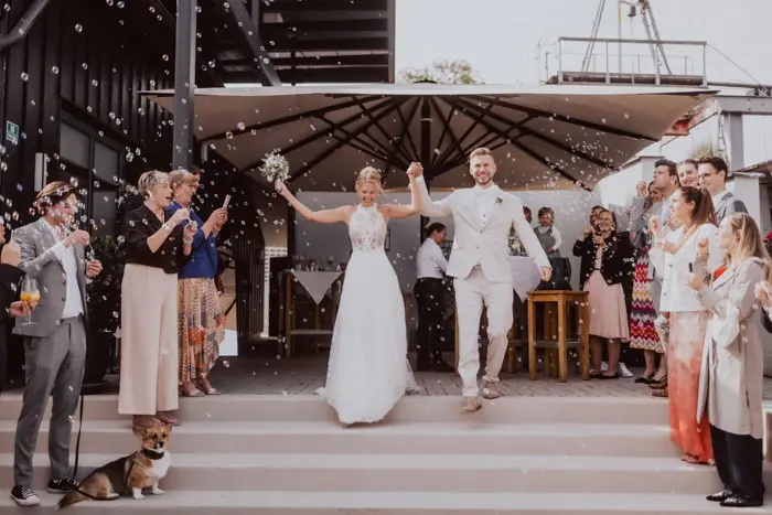 Hochzeitsfotograf Bayern Hochzeitspaar beim Auszug aus der Kirche, umgeben von jubelnden Gästen Dokumentarische Editorial Hochzeitsfotografie